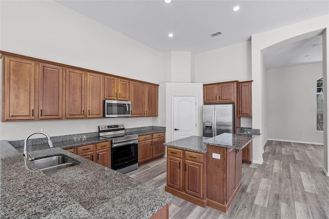 kitchen with dark stone countertops, a kitchen island, a sink, stainless steel appliances, and brown cabinets