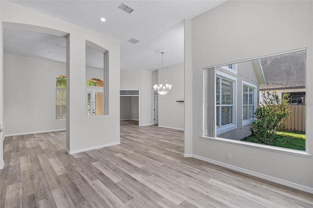 empty room featuring a chandelier, visible vents, baseboards, and wood finished floors