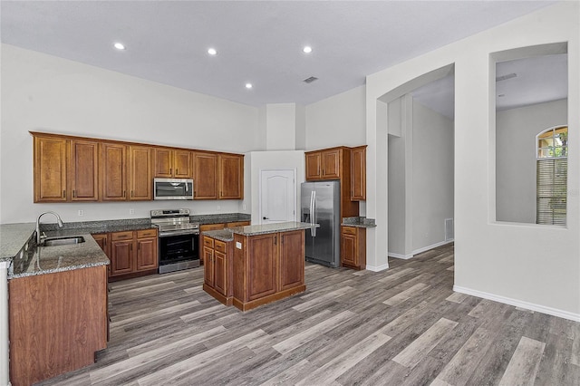 kitchen with a kitchen island, dark stone counters, brown cabinetry, stainless steel appliances, and a sink