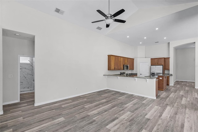 kitchen featuring visible vents, a peninsula, light wood-style floors, brown cabinetry, and stainless steel appliances