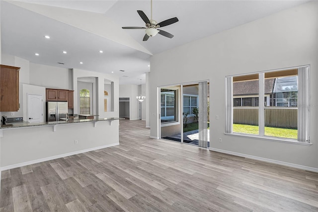 unfurnished living room with baseboards, high vaulted ceiling, and light wood finished floors