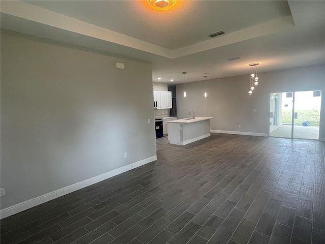 unfurnished living room with dark wood finished floors, a tray ceiling, baseboards, and visible vents