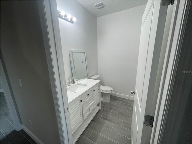 bathroom with vanity, baseboards, visible vents, a textured ceiling, and toilet