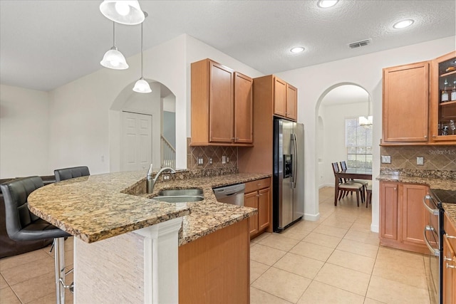 kitchen with a peninsula, arched walkways, a sink, appliances with stainless steel finishes, and a kitchen bar