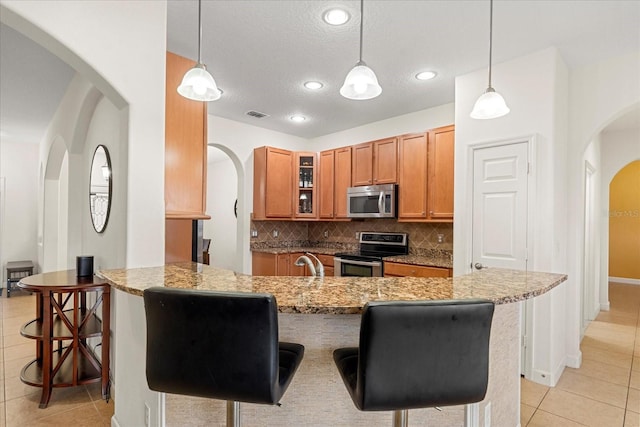 kitchen with decorative backsplash, appliances with stainless steel finishes, a peninsula, a kitchen breakfast bar, and brown cabinetry