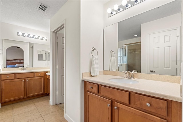 ensuite bathroom featuring tile patterned flooring, visible vents, a stall shower, a textured ceiling, and a sink