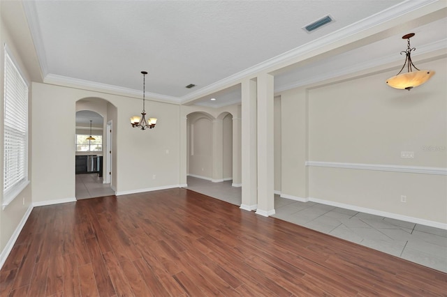 spare room featuring wood finished floors, baseboards, visible vents, arched walkways, and crown molding