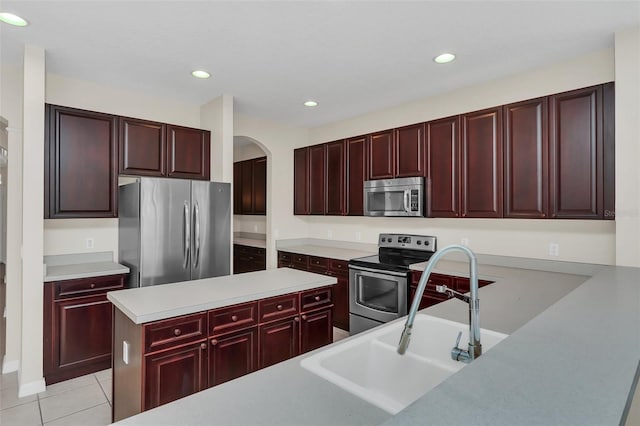 kitchen featuring light tile patterned floors, light countertops, appliances with stainless steel finishes, reddish brown cabinets, and a center island