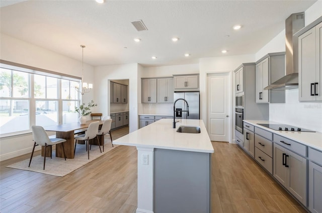 kitchen featuring visible vents, gray cabinetry, a sink, appliances with stainless steel finishes, and wall chimney exhaust hood