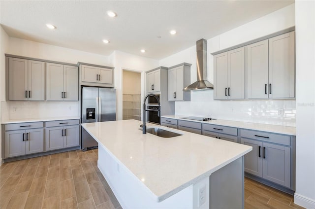 kitchen with gray cabinets, a sink, stainless steel refrigerator with ice dispenser, black electric stovetop, and wall chimney exhaust hood