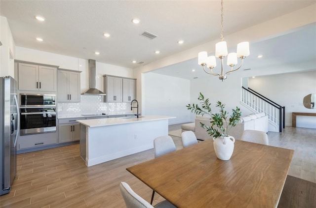 kitchen featuring visible vents, gray cabinetry, appliances with stainless steel finishes, wall chimney range hood, and backsplash