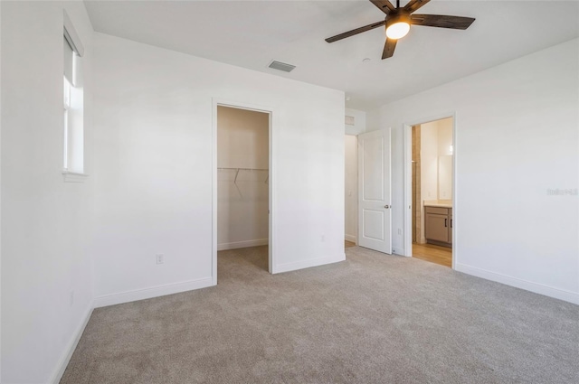 unfurnished bedroom featuring light carpet, visible vents, a walk in closet, and baseboards