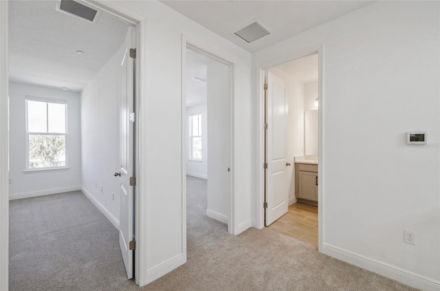 corridor with visible vents, baseboards, and light colored carpet