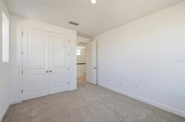 unfurnished bedroom featuring baseboards, visible vents, a closet, and light carpet