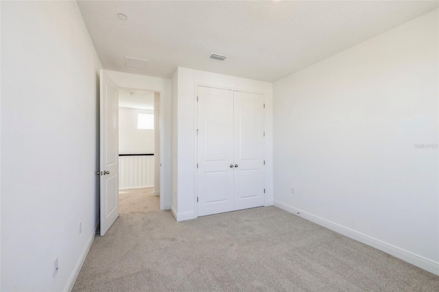 unfurnished bedroom with baseboards, visible vents, a closet, and light carpet