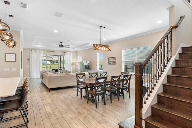 dining room featuring light wood finished floors, visible vents, stairway, a tray ceiling, and ornamental molding