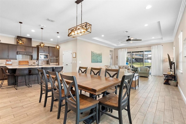 dining room featuring a ceiling fan, a raised ceiling, light wood-style floors, and visible vents