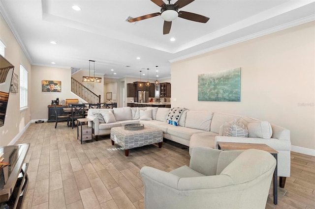 living room featuring light wood-type flooring, a tray ceiling, stairway, crown molding, and baseboards