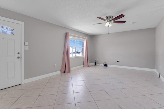 interior space featuring a textured ceiling, light tile patterned flooring, baseboards, and ceiling fan