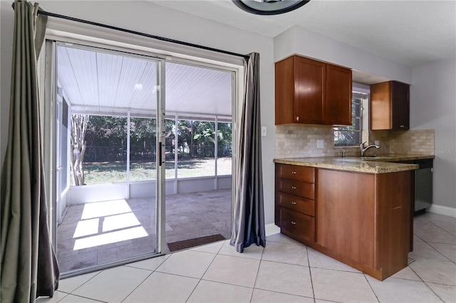 kitchen featuring decorative backsplash, light stone counters, light tile patterned flooring, and brown cabinets