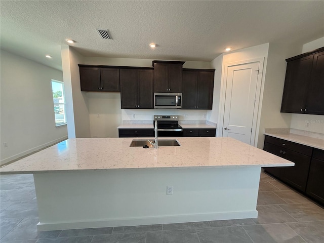 kitchen with visible vents, an island with sink, light stone counters, stainless steel appliances, and a sink