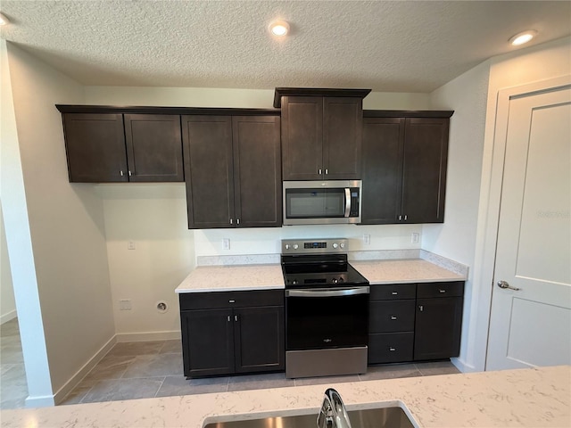 kitchen with a sink, a textured ceiling, dark brown cabinetry, appliances with stainless steel finishes, and baseboards