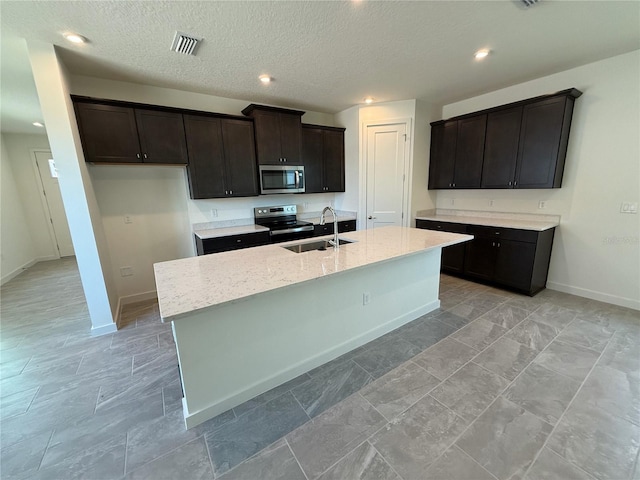 kitchen with light stone countertops, visible vents, an island with sink, a sink, and appliances with stainless steel finishes