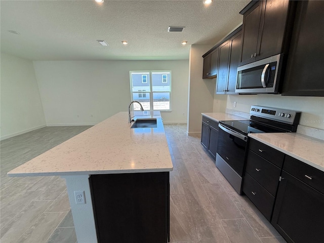 kitchen with visible vents, a kitchen island with sink, a sink, stainless steel appliances, and light stone countertops