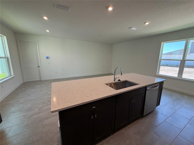 kitchen with dark cabinetry, a center island with sink, a sink, dishwasher, and open floor plan