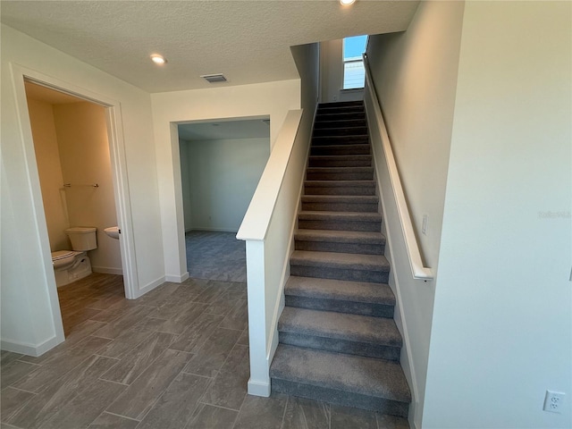 stairway with wood finished floors, baseboards, visible vents, recessed lighting, and a textured ceiling