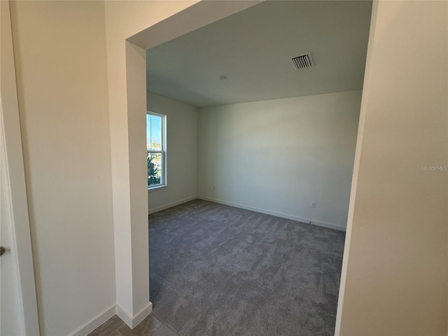 spare room featuring visible vents, dark carpet, and baseboards