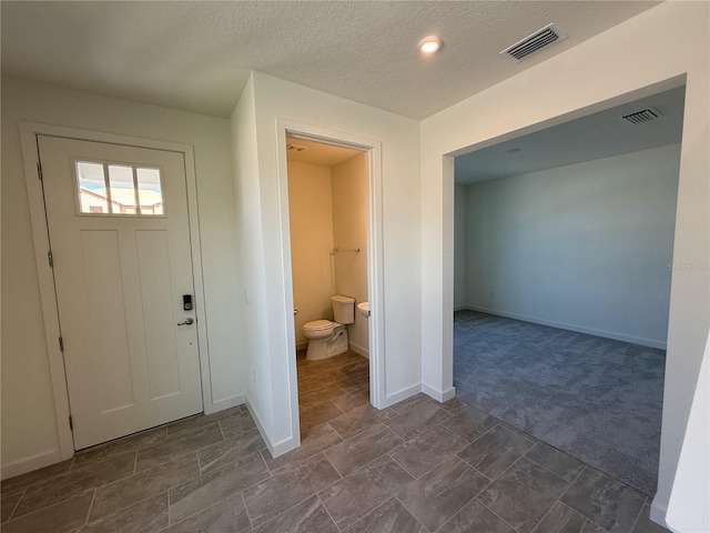 foyer featuring visible vents, a textured ceiling, baseboards, and dark colored carpet