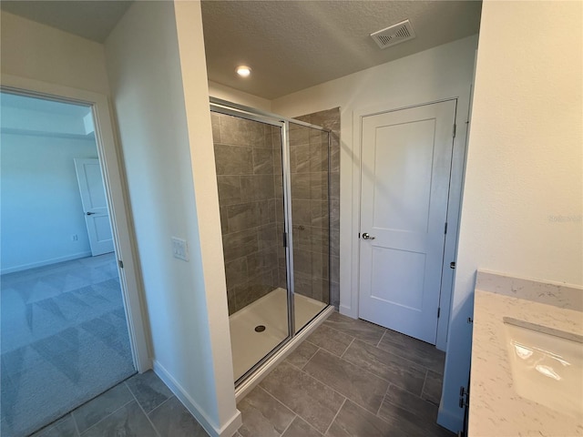 full bath with visible vents, a shower stall, a textured ceiling, and baseboards