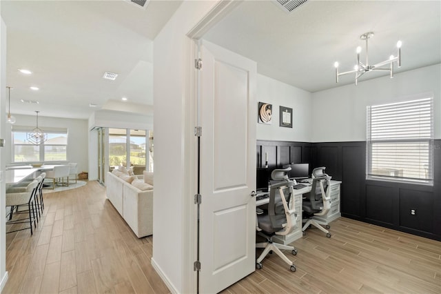 home office featuring light wood-style flooring, a notable chandelier, visible vents, and wainscoting