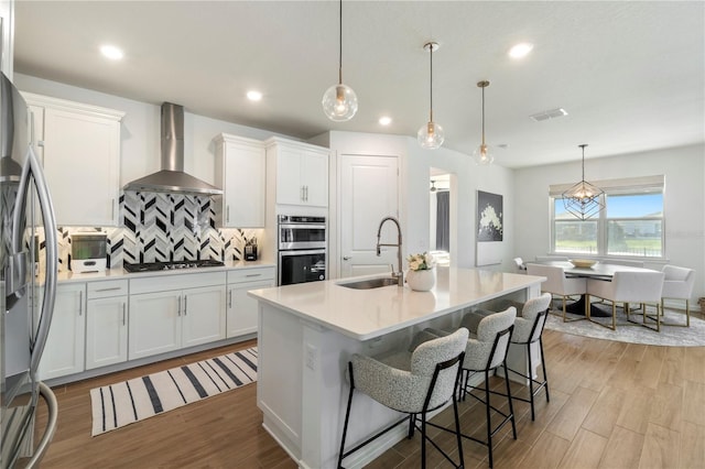 kitchen featuring visible vents, a sink, white cabinetry, stainless steel appliances, and wall chimney exhaust hood