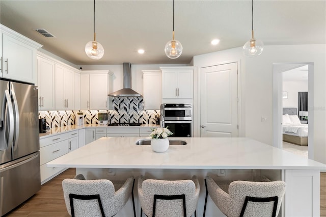 kitchen featuring visible vents, white cabinetry, appliances with stainless steel finishes, wall chimney range hood, and decorative backsplash