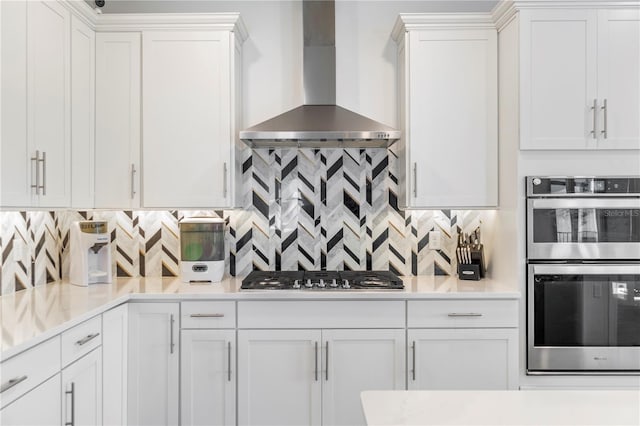 kitchen with stainless steel appliances, wall chimney exhaust hood, white cabinets, and light countertops