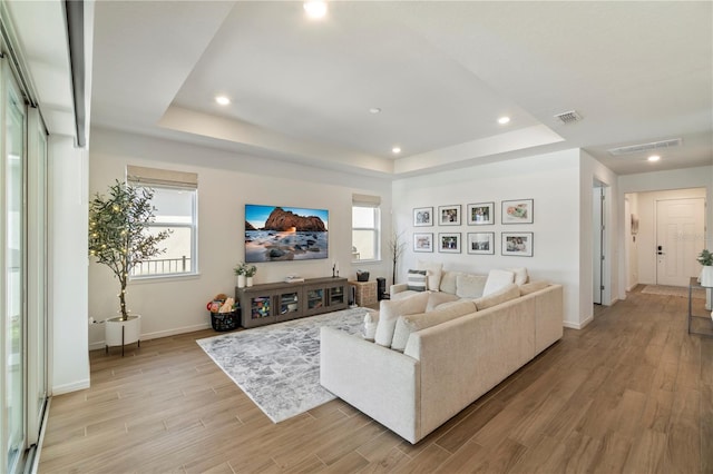 living room with visible vents, baseboards, light wood-style floors, and a tray ceiling