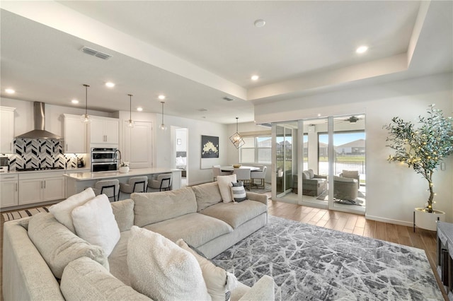 living area with visible vents, baseboards, light wood-type flooring, recessed lighting, and a raised ceiling