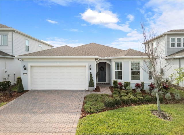 view of front of home with decorative driveway, roof with shingles, an attached garage, and stucco siding