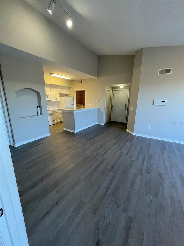 unfurnished living room with visible vents, lofted ceiling, a sink, dark wood-style floors, and baseboards