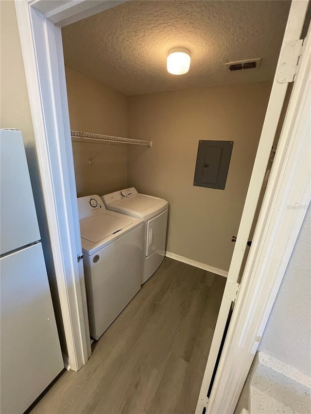 clothes washing area with washer and clothes dryer, electric panel, a textured ceiling, wood finished floors, and laundry area