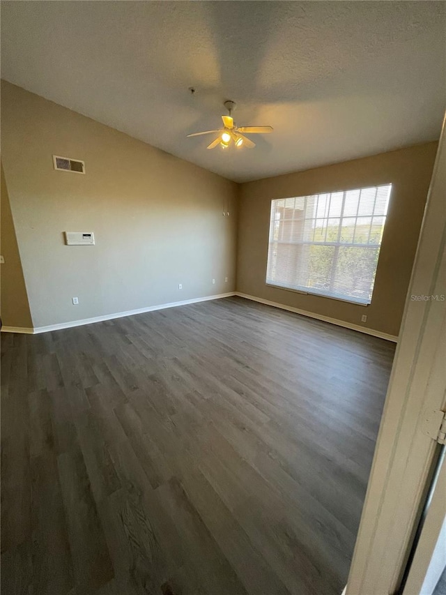 empty room featuring a ceiling fan, visible vents, baseboards, dark wood finished floors, and a textured ceiling