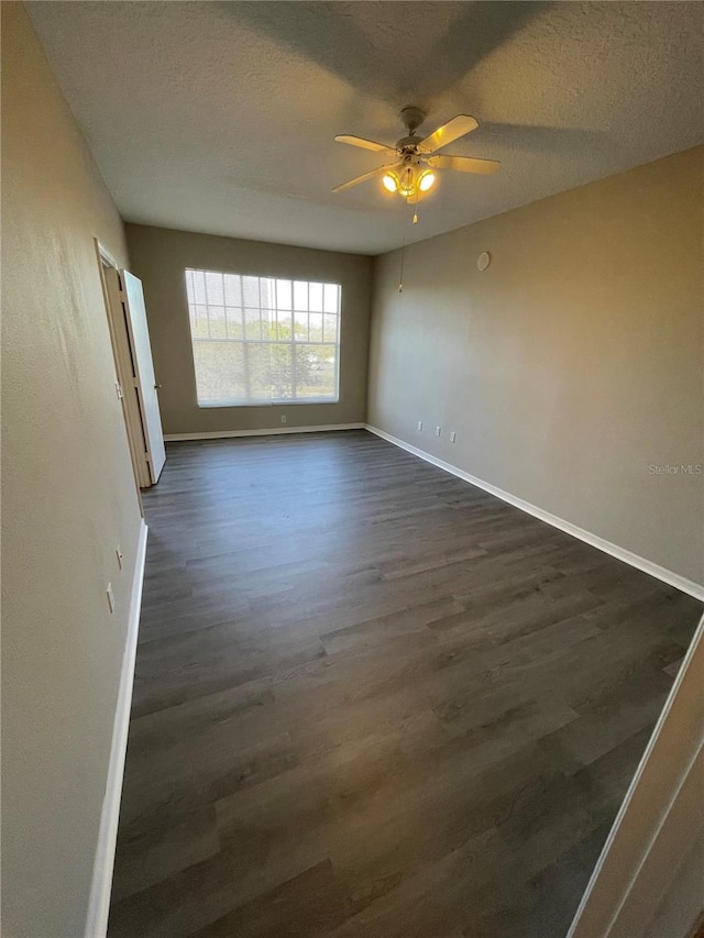 spare room with ceiling fan, baseboards, a textured ceiling, and dark wood finished floors