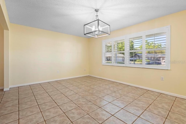 unfurnished room featuring a textured ceiling, baseboards, and a chandelier