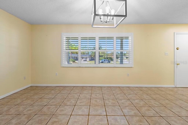 unfurnished room featuring a textured ceiling, baseboards, and a chandelier