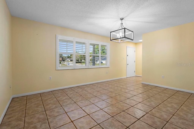 empty room with baseboards, a textured ceiling, and an inviting chandelier