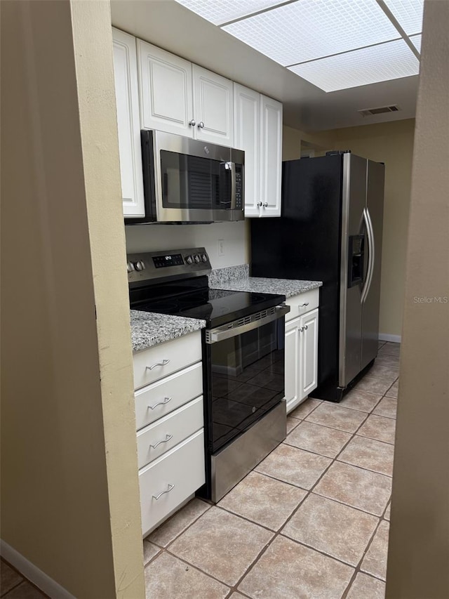 kitchen featuring light stone counters, appliances with stainless steel finishes, white cabinets, light tile patterned floors, and baseboards