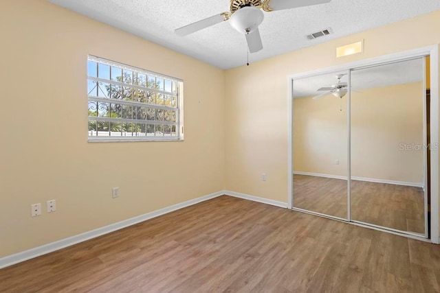unfurnished bedroom with a closet, visible vents, a textured ceiling, and wood finished floors