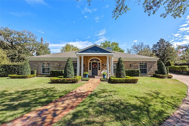 neoclassical / greek revival house featuring brick siding, a chimney, and a front yard